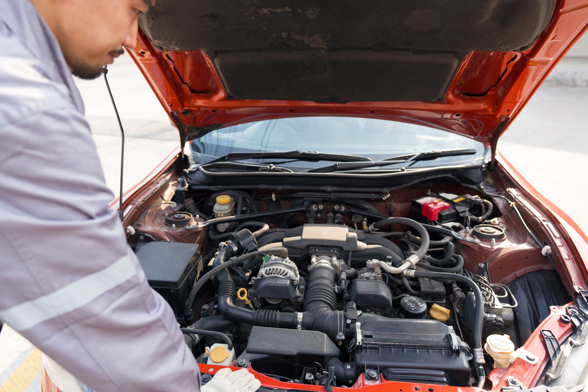 A mechanic in uniform and protective glove looks at a sport car's engine to fix it. Working atmosphere at car repair shop.
